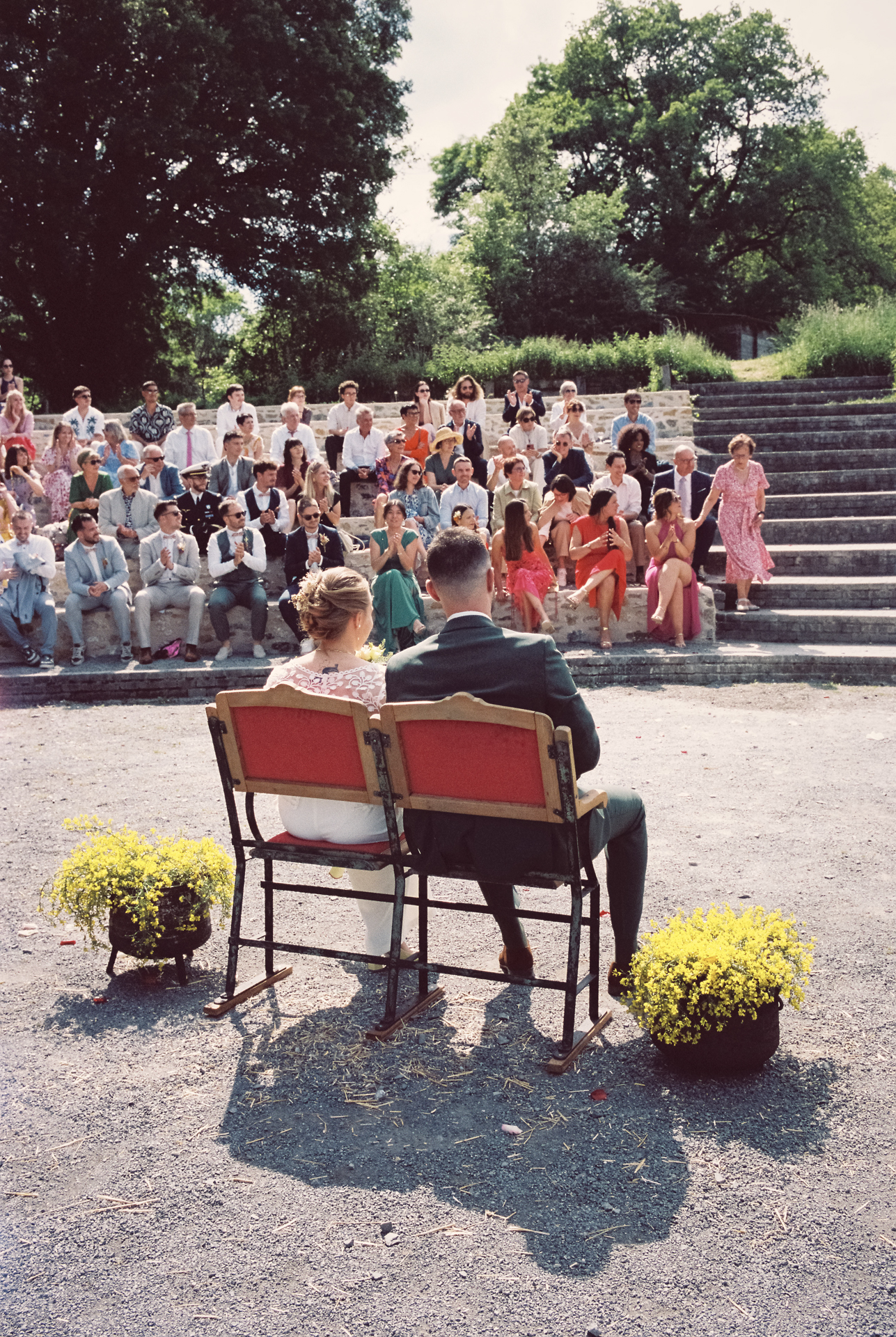 Mariés assis face à leurs invités pendant une cérémonie de mariage en extérieur, photo prise à l'appareil photo argentique