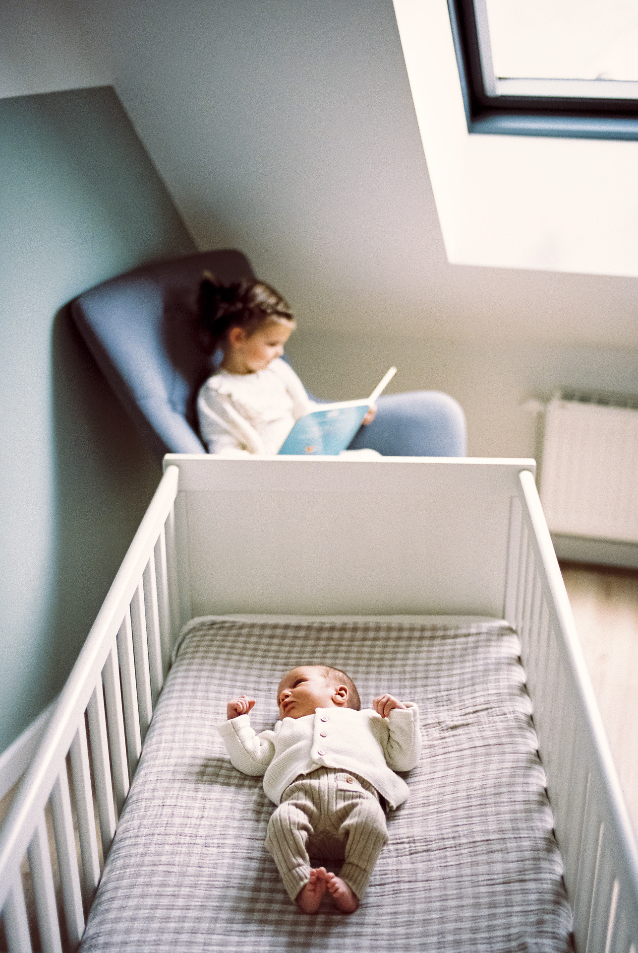 Nouveau-né dans son lit pendant que sa grande sœur lit dans la chambre