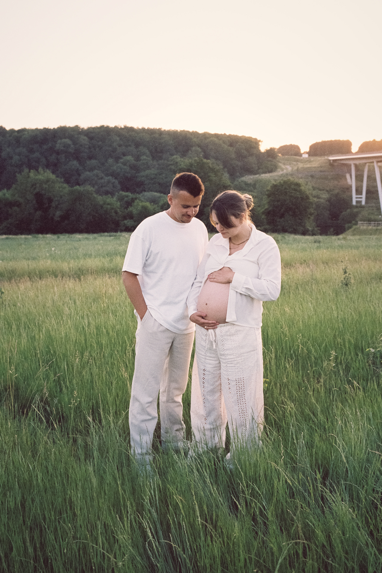 Couple attendant un bébé photographié dans un champ pendant une séance grossesse en extérieur