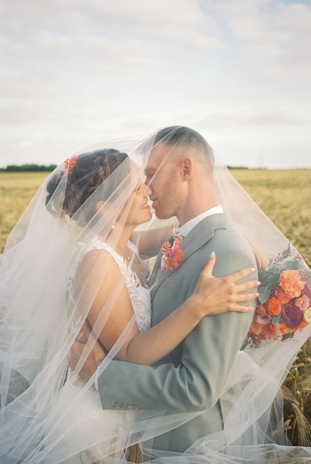 Couple de mariés enlacé sous le voile dans un champ lors de leur mariage au Petit Vilami